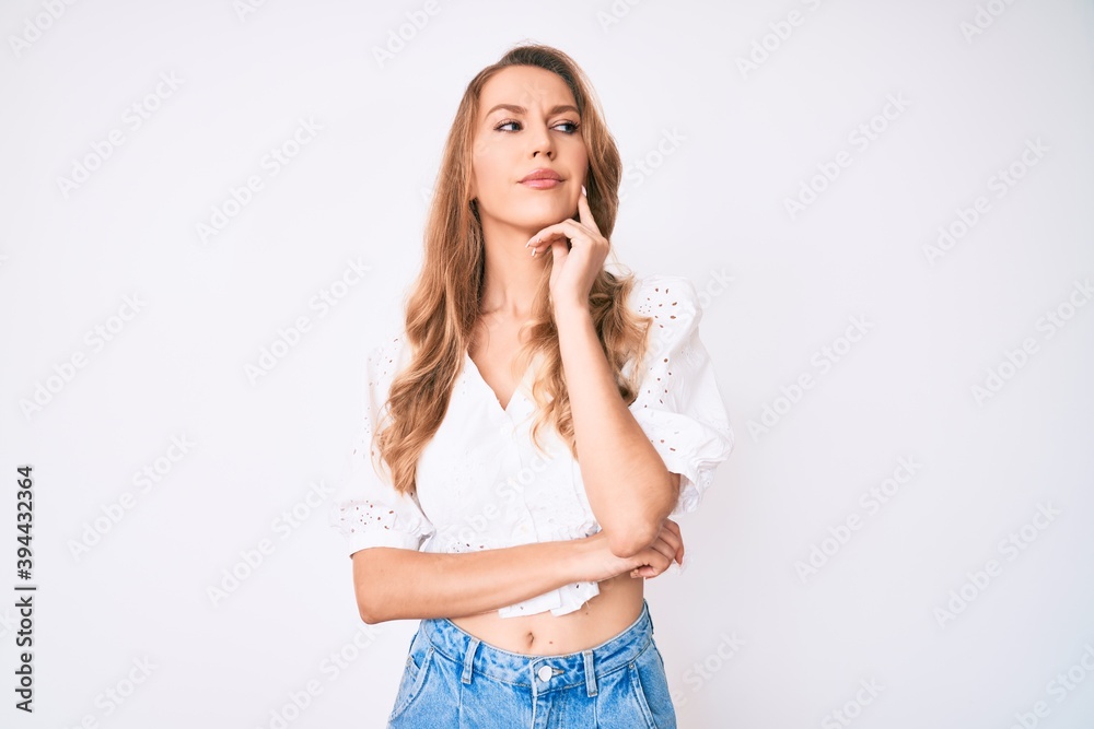 Young caucasian woman with blond hair wearing casual summer clothes serious face thinking about question with hand on chin, thoughtful about confusing idea Young caucasian woman with blond hair wearing casual summer clothes serious face thinking about question with hand on chin, thoughtful about confusing idea