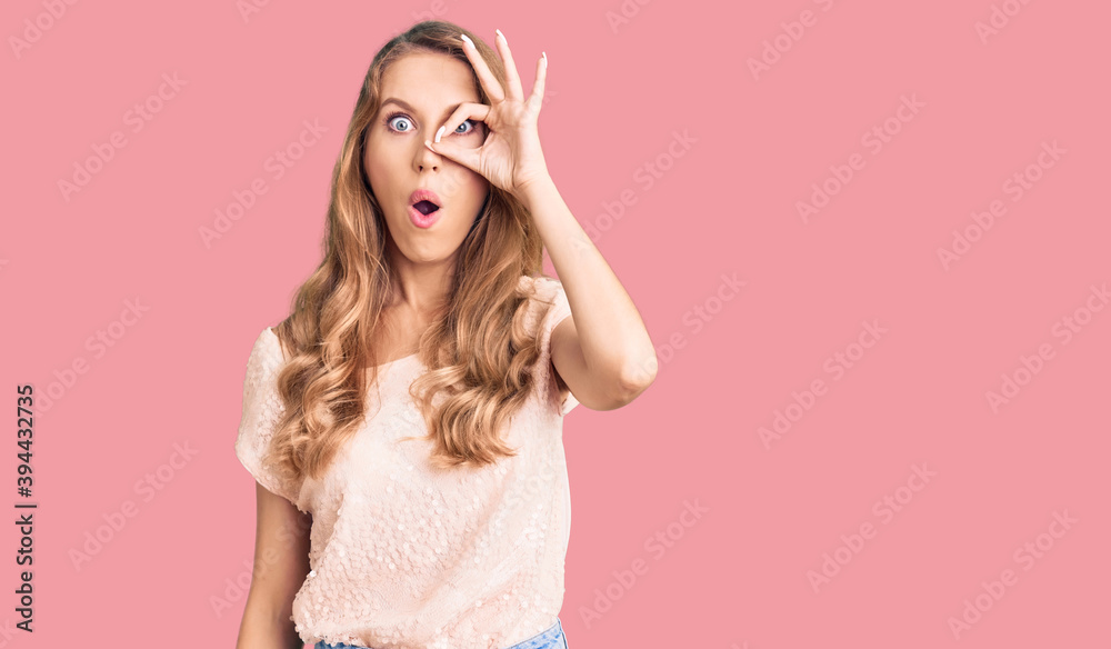 Young beautiful caucasian woman with blond hair wearing casual clothes doing ok gesture shocked with surprised face, eye looking through fingers. unbelieving expression. Young beautiful caucasian woman with blond hair wearing casual clothes doing ok gesture shocked with surprised face, eye looking through fingers. unbelieving expression.