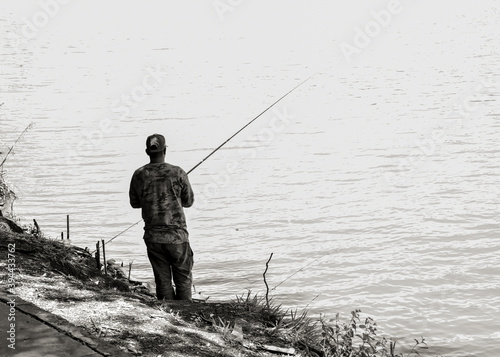 Black and white. Back view of a man fishing in the lake.