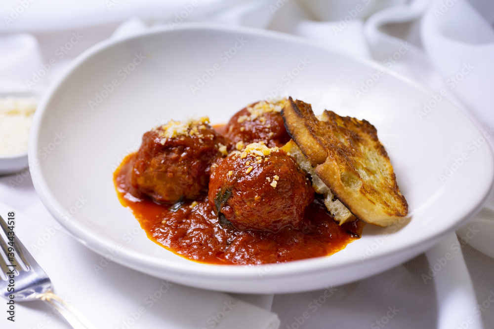 A view of a plate of meatballs, marinara and a slice of garlic bread, in a restaurant or kitchen setting. A view of a plate of meatballs, marinara and a slice of garlic bread, in a restaurant or kitchen setting.