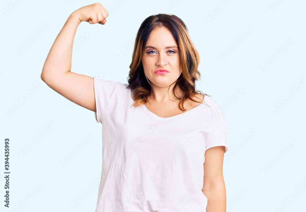 Young beautiful caucasian woman wearing casual white tshirt strong person showing arm muscle, confident and proud of power Young beautiful caucasian woman wearing casual white tshirt strong person showing arm muscle, confident and proud of power