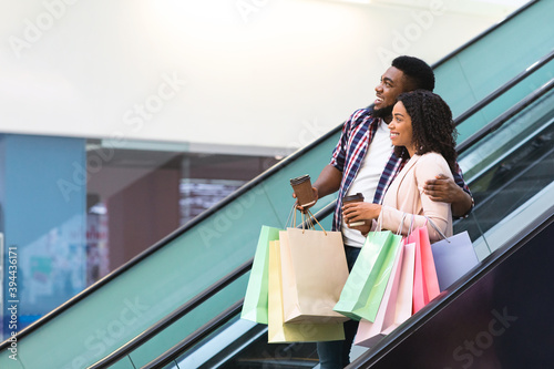 Happy african couple riding escalator in shopping mall, enjoying making purchases together
