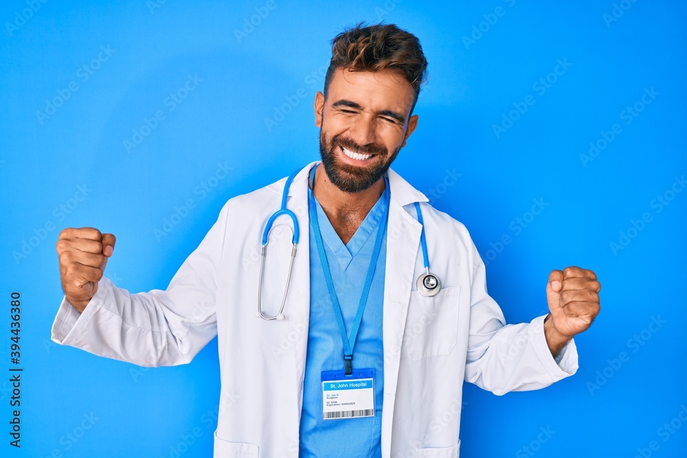 Young hispanic man wearing doctor uniform and stethoscope very happy and excited doing winner gesture with arms raised, smiling and screaming for success. celebration concept. Young hispanic man wearing doctor uniform and stethoscope very happy and excited doing winner gesture with arms raised, smiling and screaming for success. celebration concept.