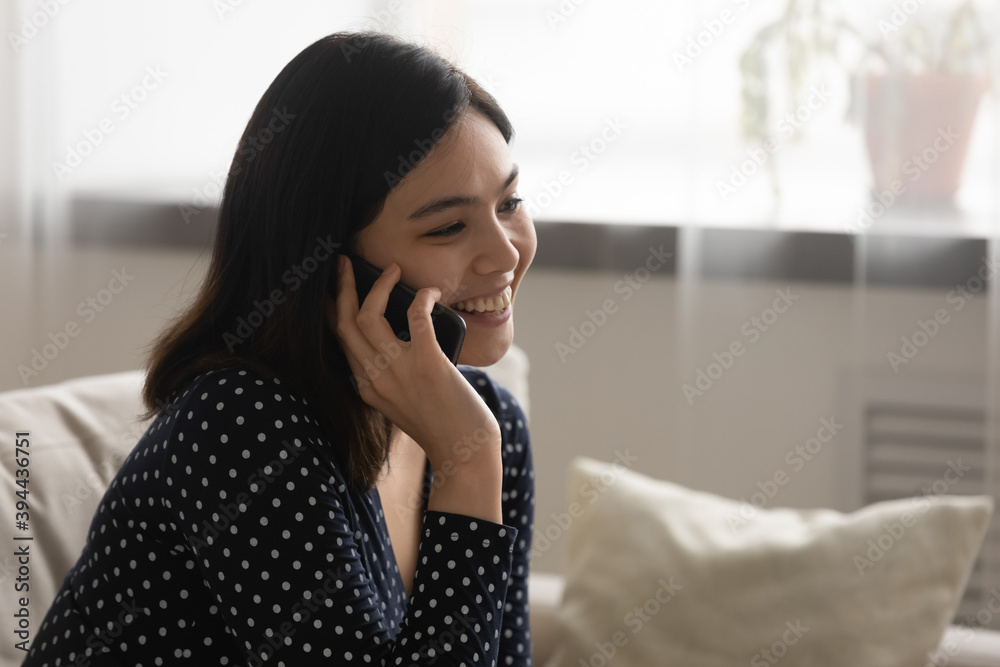 Close up smiling Asian young woman talking on phone, chatting with friend or boyfriend, sitting on cozy couch at home, happy girl holding smartphone, making call, having pleasant conversation Close up smiling Asian young woman talking on phone, chatting with friend or boyfriend, sitting on cozy couch at home, happy girl holding smartphone, making call, having pleasant conversation