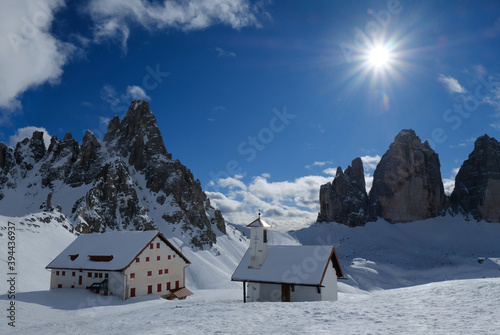 Beautiful panorama of Tre Cime di Lavaredo and Monte Paterno in sunny winter scenery. Refuge and chapel at foot of mountains. Dolomites  Italy