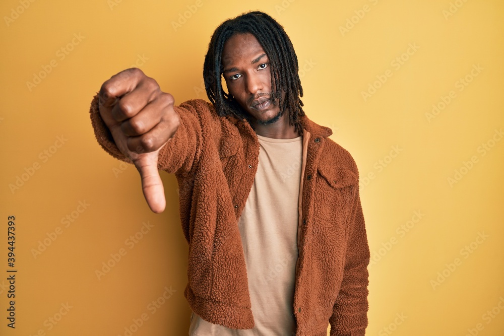 African american man with braids wearing brown retro jacket looking unhappy and angry showing rejection and negative with thumbs down gesture. bad expression. African american man with braids wearing brown retro jacket looking unhappy and angry showing rejection and negative with thumbs down gesture. bad expression.