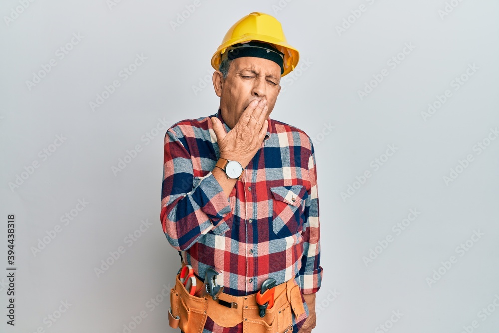 Handsome senior man with grey hair wearing handyman uniform and safety hat smiling with happy face looking and pointing to the side with thumb up.