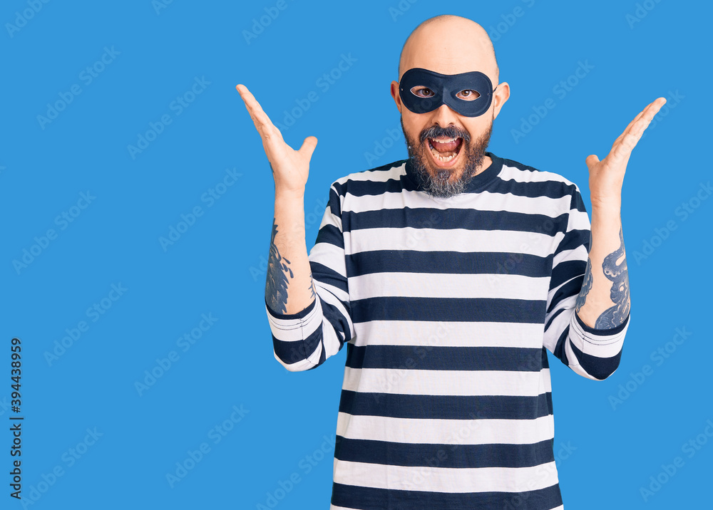 Naklejka premium Young handsome man wearing burglar mask celebrating crazy and amazed for success with arms raised and open eyes screaming excited. winner concept