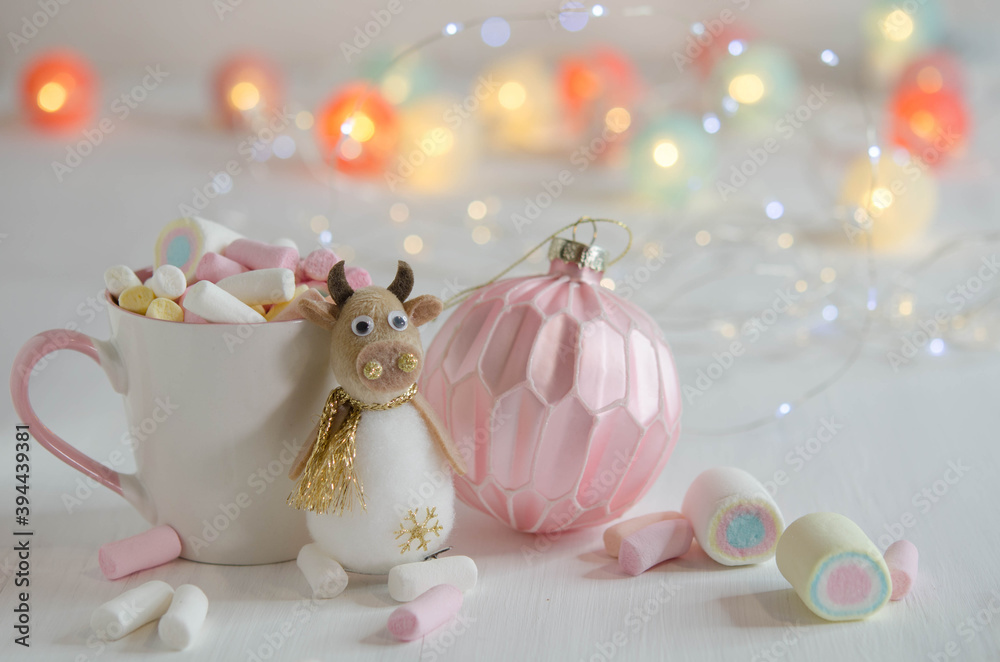 White cup with marshmallows and a toy bull on a blurred background. White cup with marshmallows and a toy bull on a blurred background.