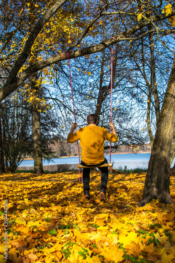 Fototapeta premium Photo of a young blonde woman on a swing in the middle of the woods in an autumn day. Vilnius.