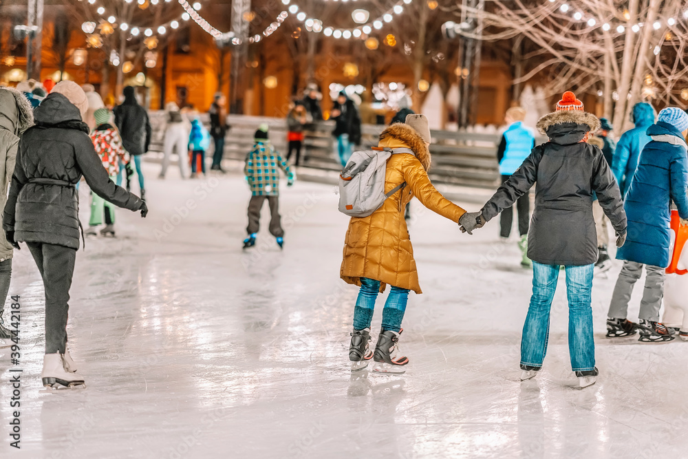 Happy couples, friends ice skate on a skating rink in a city park together. Healthy winter outdoor activities