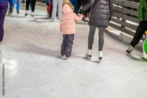 Mom teaches doughter together to skate, evening time outdoors in the Ice rink of park. Winter activities and sport concept.