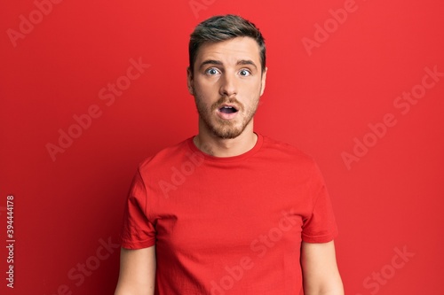 Handsome caucasian man wearing casual red tshirt afraid and shocked with surprise and amazed expression, fear and excited face.