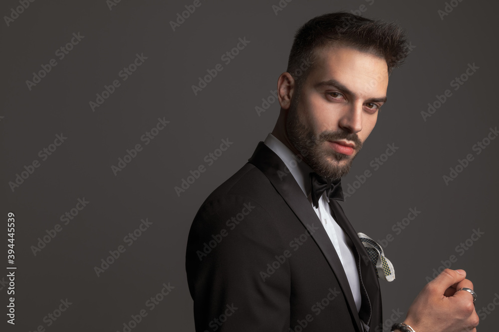 Fototapeta premium side view of attractive groom in black tuxedo posing