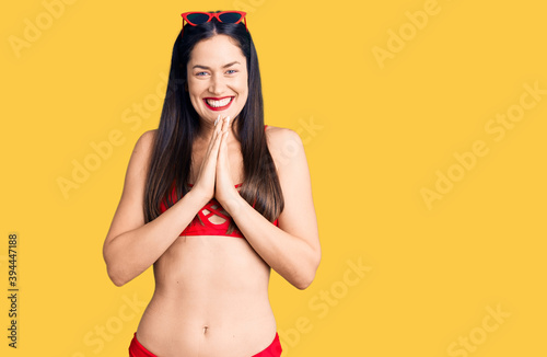 Young beautiful caucasian woman wearing bikini praying with hands together asking for forgiveness smiling confident. photo