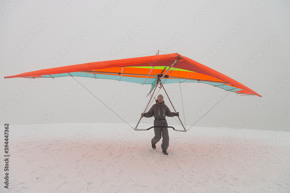 Girl run on snow with colorful hang glider wing.