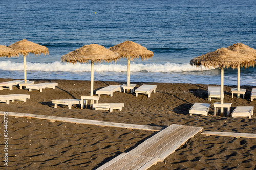Sun loungers on the black volcanic sand beach of Perissa, a tourist resort in Santorini. Cyclades, Greece © vivoo