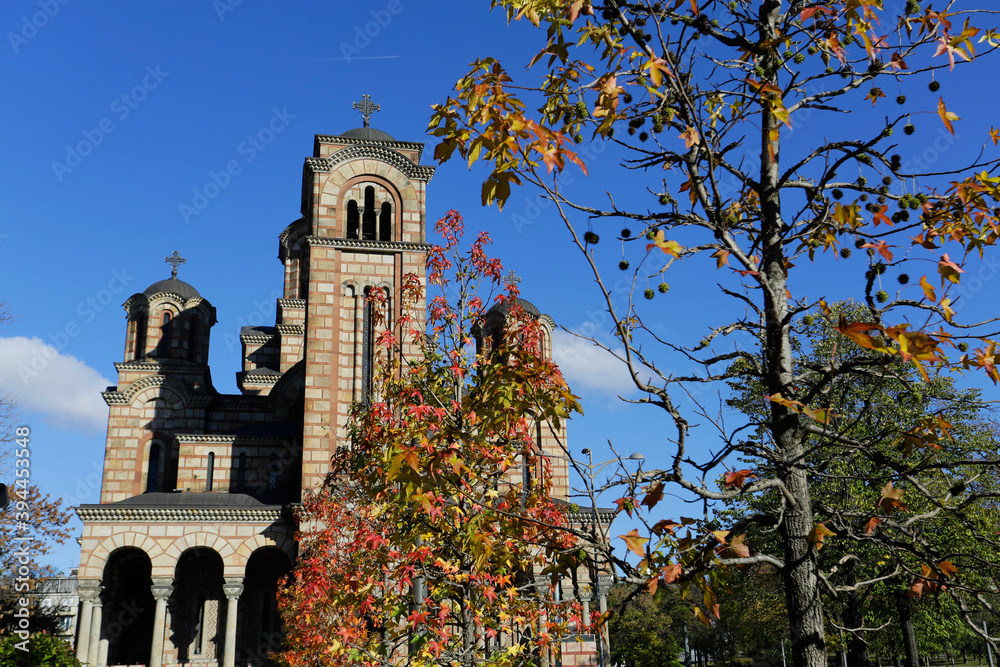 Front view of St. Mark's orthodox church amid colorful trees in Tasmajdan park, during a sunny autumn day in Belgrade, Serbia.