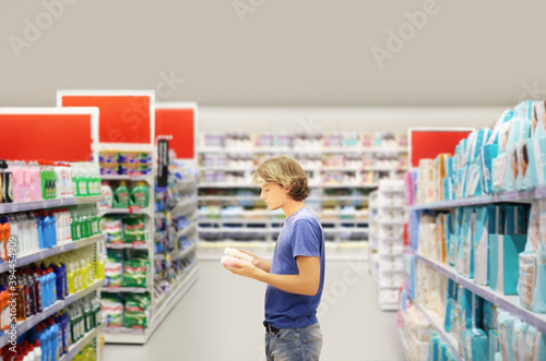 Man shopping in supermarket reading product information.(washing powder,detergent,soap,shampoo).
