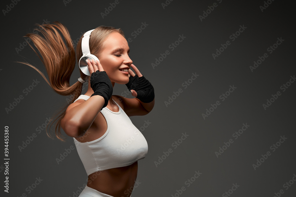 Obraz premium Woman with perfect abs wearing headphones and white clothes standing in gym isolated grey background.