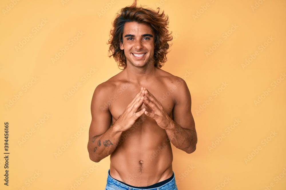 Fototapeta premium Young hispanic man standing shirtless hands together and fingers crossed smiling relaxed and cheerful. success and optimistic