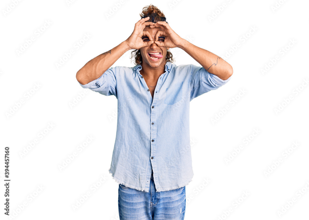 Young hispanic man wearing summer style doing ok gesture like binoculars sticking tongue out, eyes looking through fingers. crazy expression. Young hispanic man wearing summer style doing ok gesture like binoculars sticking tongue out, eyes looking through fingers. crazy expression.
