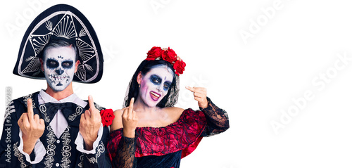 Young couple wearing mexican day of the dead costume over background showing middle finger doing fuck you bad expression, provocation and rude attitude. screaming excited