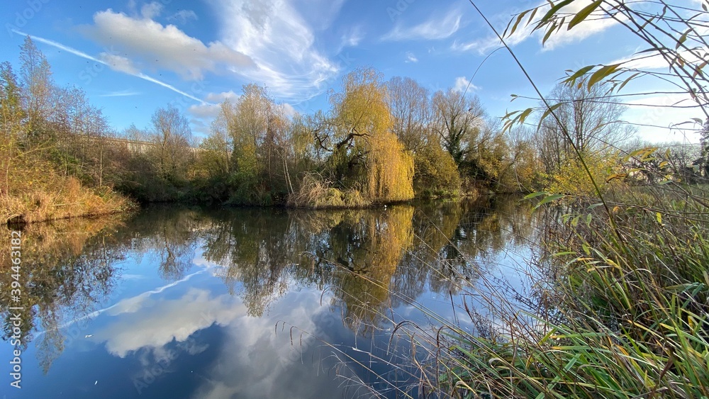 Park canal in a beautiful sunny autumn day with trees and cloud reflecting on the calm, still water, scenic nature landscape, beautiful nature, blue sky and water. Park canal in a beautiful sunny autumn day with trees and cloud reflecting on the calm, still water, scenic nature landscape, beautiful nature, blue sky and water.