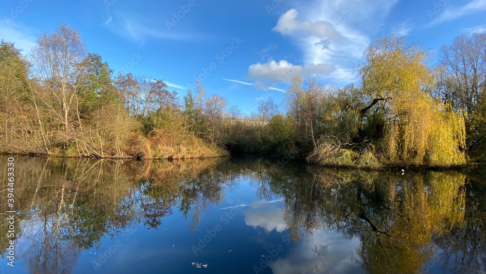 Park canal in a beautiful sunny autumn day with trees and cloud reflecting on the calm, still water, scenic nature landscape, beautiful nature, blue sky and water. Park canal in a beautiful sunny autumn day with trees and cloud reflecting on the calm, still water, scenic nature landscape, beautiful nature, blue sky and water.