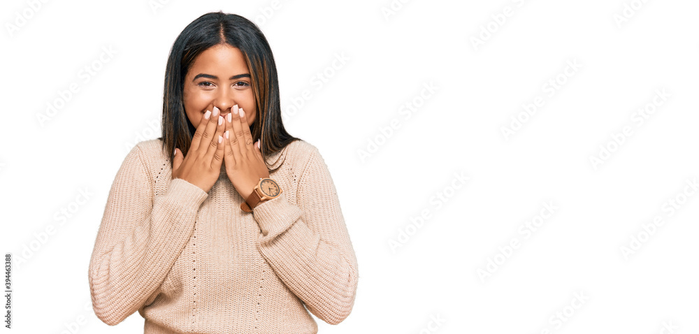 Young latin girl wearing wool winter sweater laughing and embarrassed giggle covering mouth with hands, gossip and scandal concept Young latin girl wearing wool winter sweater laughing and embarrassed giggle covering mouth with hands, gossip and scandal concept