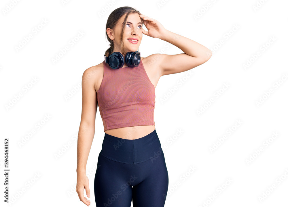 Beautiful caucasian young woman wearing gym clothes and using headphones smiling confident touching hair with hand up gesture, posing attractive and fashionable Beautiful caucasian young woman wearing gym clothes and using headphones smiling confident touching hair with hand up gesture, posing attractive and fashionable