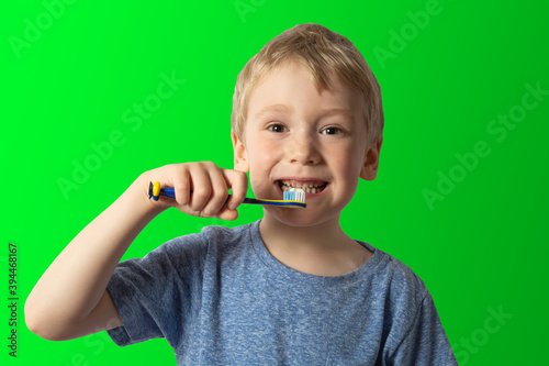 a boy with white hair holds a toothbrush in his hands wants to brush his teeth. green background.