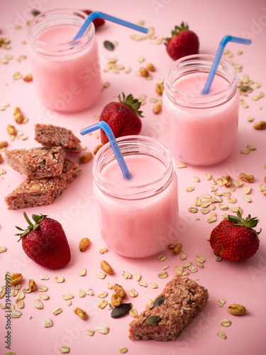 Healthy sweet dessert snack and breakfast. Cereal granola bar with nuts and strawberries and strawberry milkshake on a pink background.