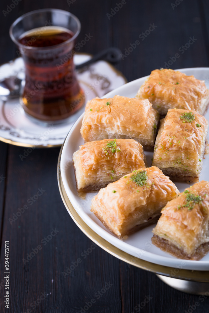 Turkish baklava in white plate with glass of tea in New year setting or decoration on dark wooden background