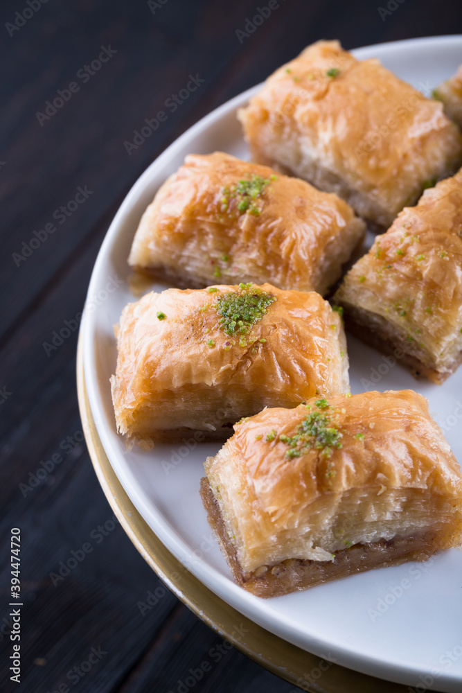 Traditional Turkish baklava in white plate on wooden background, east Mediterranean cuisine, served with black tea Traditional Turkish baklava in white plate on wooden background, east Mediterranean cuisine, served with black tea
