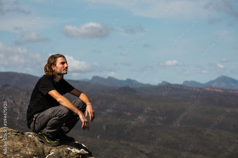 Handsome young traveler man hiking in the mountain, looking to the horizon. Sportive guy on top of the mountain enjoying great landscape. Concept about travel, lifestyle, sport, nature and people. 