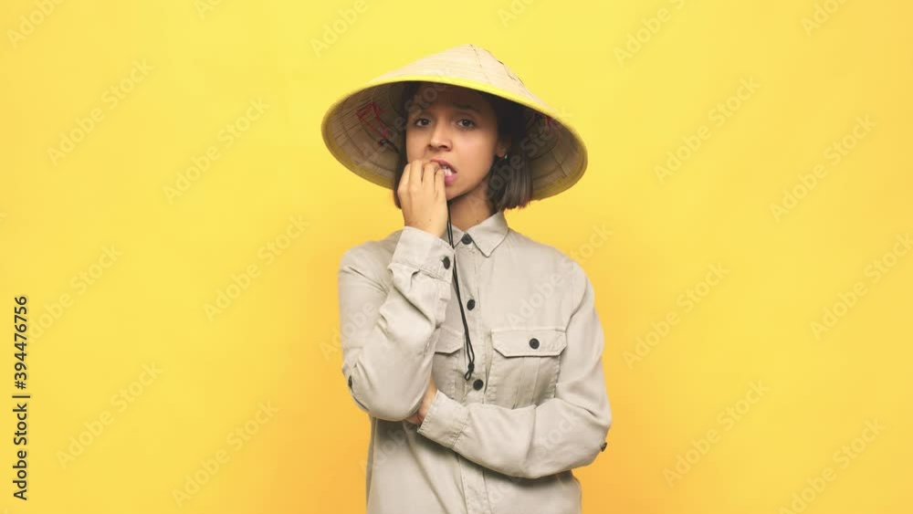 Young latin woman with vietnamite hat biting fingernails, nervous and very anxious Young latin woman with vietnamite hat biting fingernails, nervous and very anxious