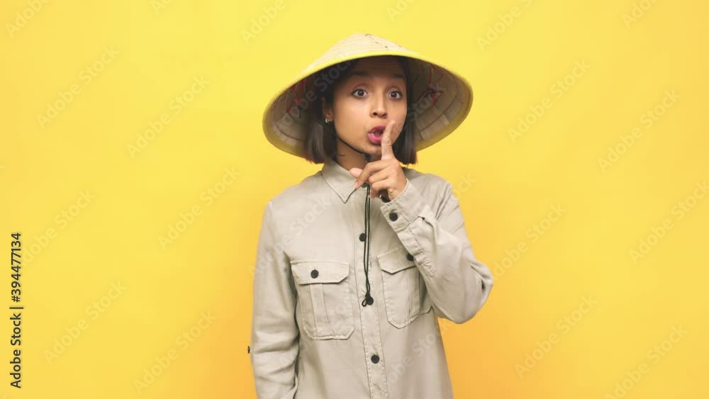 Young latin woman with vietnamite hat keeping a secret or asking for silence Young latin woman with vietnamite hat keeping a secret or asking for silence