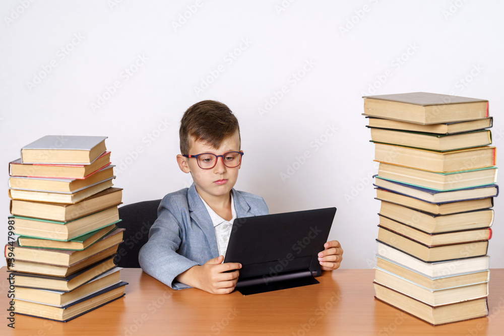 The student does homework using a tablet. He has books on both sides. The student does homework using a tablet. He has books on both sides.