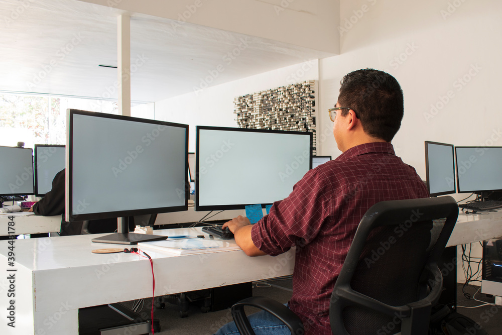 A latin man with glasses, probably an architect or a entrepreneur writing in computer in a office, dressing informal clothes A latin man with glasses, probably an architect or a entrepreneur writing in computer in a office, dressing informal clothes