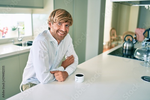 Young irish man smiling happy drinking cup of coffee sitting on the table at home.