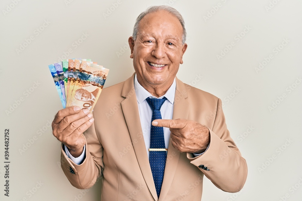 Senior caucasian man holding canadian dollars smiling happy pointing with hand and finger Senior caucasian man holding canadian dollars smiling happy pointing with hand and finger