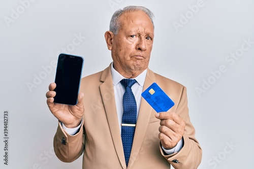 Senior caucasian man holding smartphone and credit card skeptic and nervous, frowning upset because of problem. negative person. © Krakenimages.com