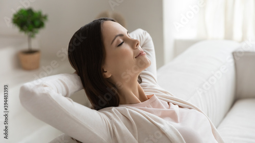 Weekend, at least .. Tranquil peaceful millennial female enjoying freedom napping dreaming relaxing on couch with closed eyes and hands behind head meditating breathing fresh air feeling happy serene