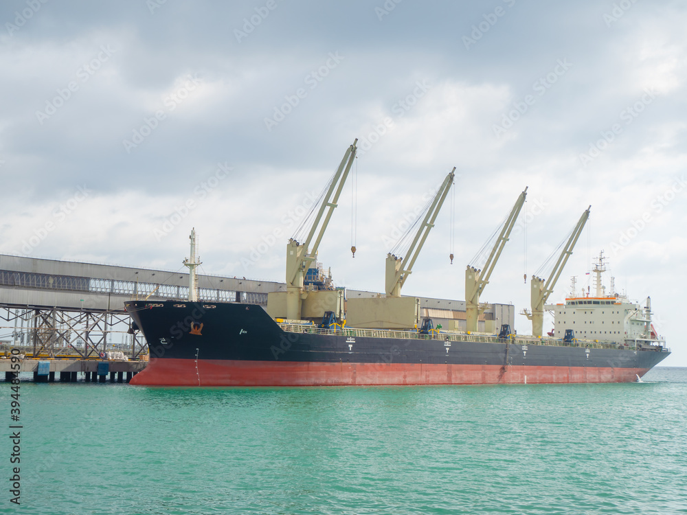 A huge cargo ship with cranes on it is moored at sea to the pier