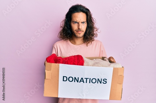 Young handsome man with long hair holding donations box for charity skeptic and nervous, frowning upset because of problem. negative person. © Krakenimages.com
