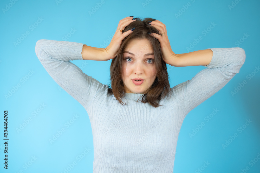 Young pretty woman feeling stressed, worried, anxious or scared, with hands on head, panicking at mistake over blue background.