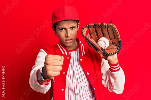 Young african amercian man wearing baseball uniform holding golve and ball annoyed and frustrated shouting with anger, yelling crazy with anger and hand raised photo