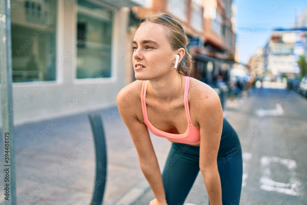 Young blonde sportswoman tired resting with hands on knees at the city. Young blonde sportswoman tired resting with hands on knees at the city.