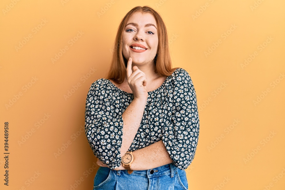Young beautiful redhead woman wearing shirt with floral print smiling looking confident at the camera with crossed arms and hand on chin. thinking positive. Young beautiful redhead woman wearing shirt with floral print smiling looking confident at the camera with crossed arms and hand on chin. thinking positive.